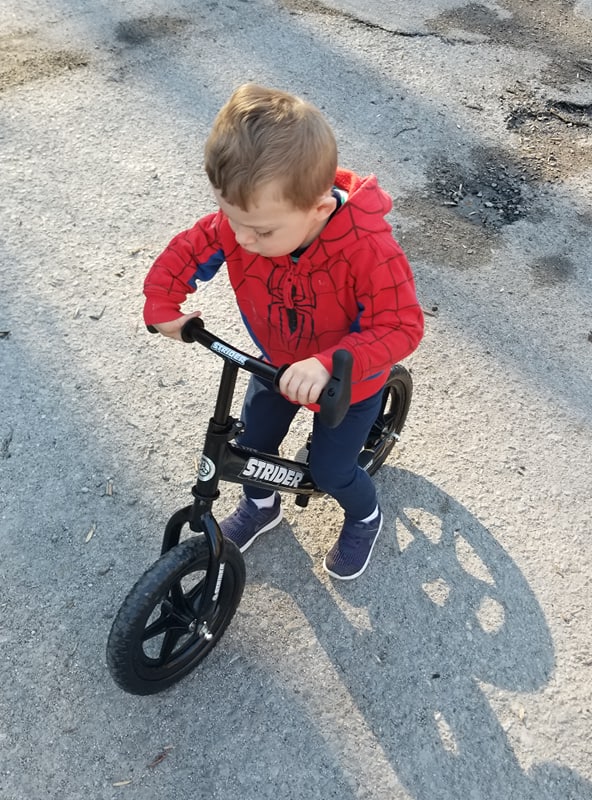 Caden Mollohan with right radial aplasia stands on his adaptive 12" Strider Classic bike