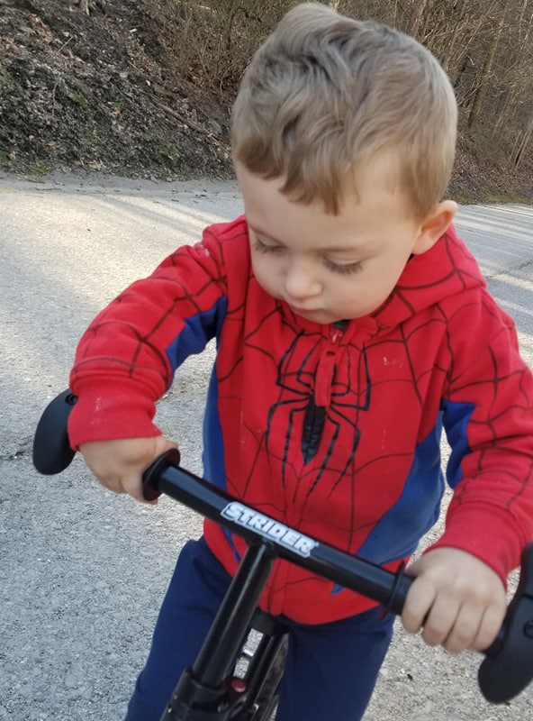 Caden Mollohan with right radial aplasia stands on his adaptive 12" Strider Classic bike